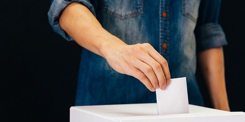 Front view of person holding ballot paper casting vote at a polling station for election vote in black background